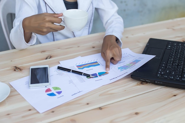 Midsection of woman with coffee analyzing charts on office desk