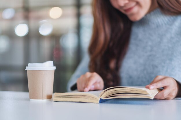 Midsection of woman with coffee cup while reading book on table