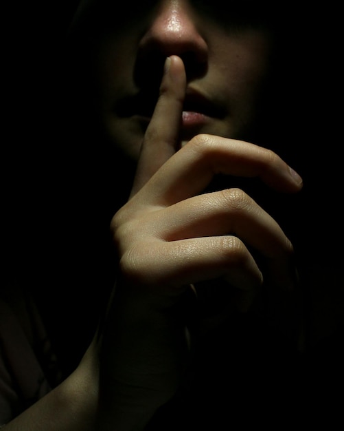 Midsection of woman with finger on lips in darkroom