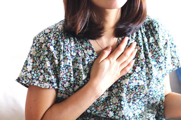 Midsection of woman with hand on chest standing against wall