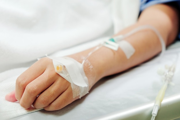 Midsection of woman with iv drip lying on bed in hospital