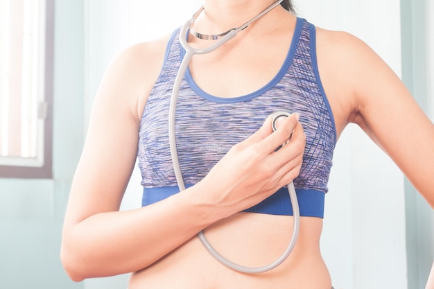 Photo midsection of woman with stethoscope examining herself against wall