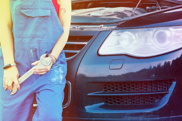 Foto sezione centrale di una donna con la chiave inglese appoggiata all'auto