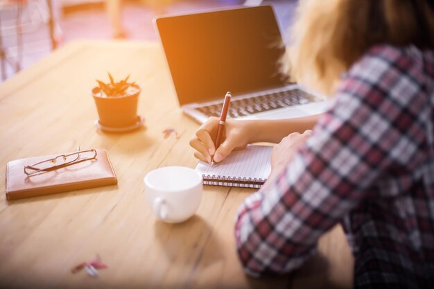 Foto sezione centrale di una donna che scrive in un libro con un portatile sul tavolo