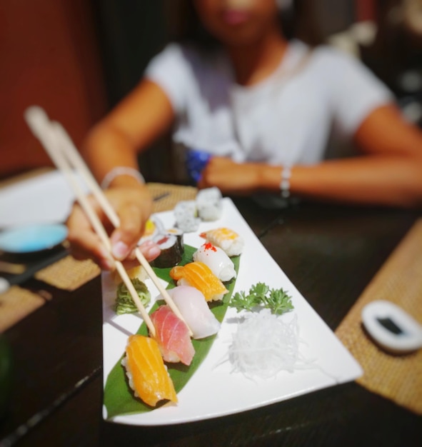 Foto sezione centrale di una giovane ragazza che tiene il sushi sul tavolo in un ristorante