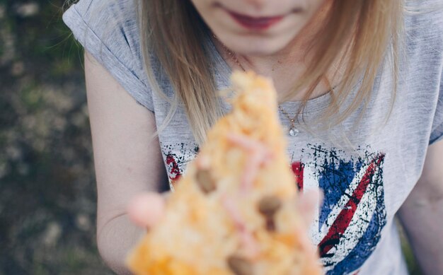 Foto sezione centrale di una giovane donna che mangia la pizza in piedi all'aperto