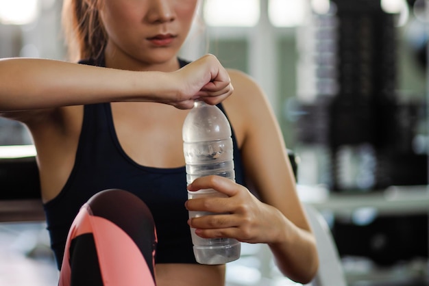 Foto sezione centrale di una giovane donna con una bottiglia d'acqua in palestra