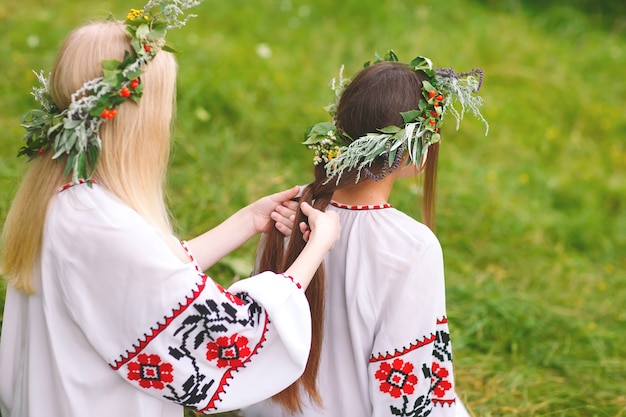 Фото В середине лета. две девушки в славянской одежде плетут косы в волосы