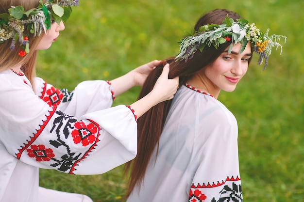 Midsummer. Two girls in the Slavic clothes weave braids in the hair