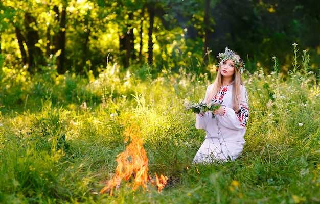 Metà estate, donna che tesse una corona vicino al fuoco.