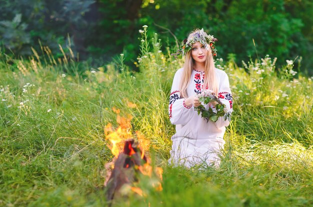 Midsummer. Woman weaving a wreath near the fire.