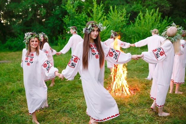 В середине лета. Молодежь в славянской одежде кружится вокруг костра в летнее время. .