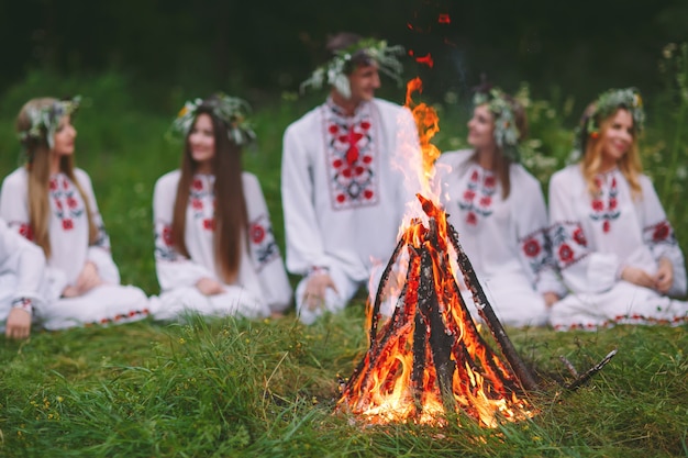 В середине лета. Молодые люди в славянской одежде сидят в лесу у костра.