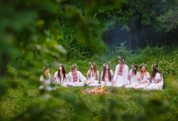 Midzomer, jonge mensen in Slavische kleding zitten in het bos bij het vuur.