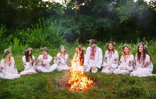 Midzomer, jonge mensen in slavische kleding zitten in het bos bij het vuur.