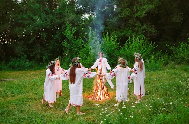 Midzomer. Jongeren in Slavische kleren dansen rond een kampvuur in het bos.