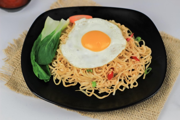 Mie Goreng Fried noodles served with fried eggs and vegetables on a plate