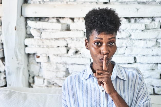 A miggleaged african woman sitting on her sofa keeping a secret or asking for silence