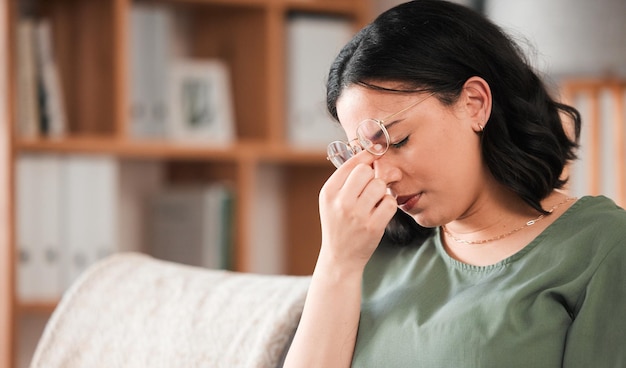 Migraine stress en jonge vrouw in haar woonkamer met een burn-out of geestelijke gezondheidsprobleem hoofdpijn vermoeide en uitgeputte vrouw zit op een bank in de woonkamer van haar moderne appartement