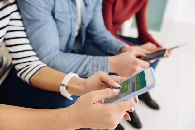 Foto mijn apparaat. drie vrienden zittend op de bank en smartphones in handen houden tijdens het online chatten