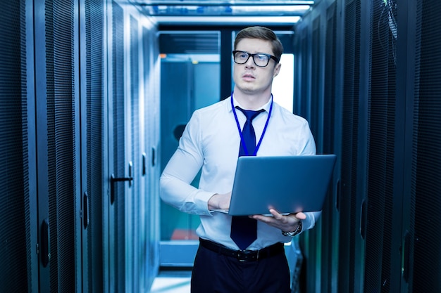 Foto mijn beroep. intelligente jonge werknemer die zijn laptop vasthoudt terwijl hij in het datacenter werkt