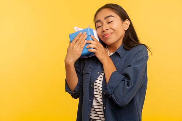 Mijn beste cadeau portret van charmant gelukkig meisje in denim shirt omarmen haar verjaardagscadeau strak glimlachend met plezier op zoek tevreden dromerige indoor studio shot geïsoleerd op gele achtergrond