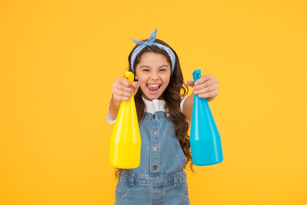 Mijn huis is op mijn manier schoongemaakt Gelukkig klein meisje maakt huis schoon op gele achtergrond Kleine huisbewaarder houdt spuitflessen Huis in de hand van schoonmaakservice Huishoudelijke taken