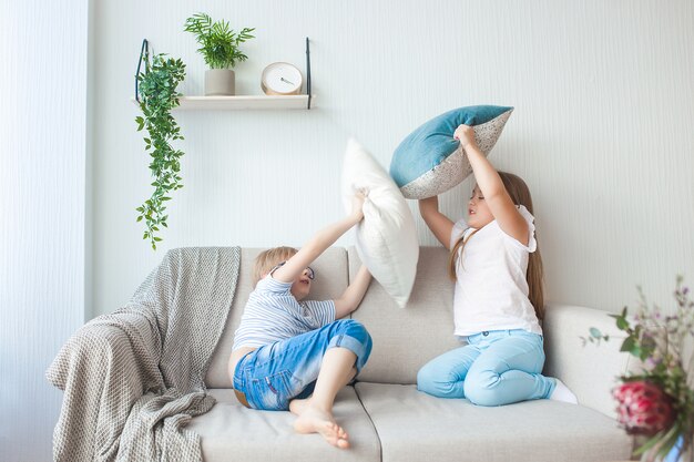 Mijn lieve kinderen hebben plezier binnenshuis. Kinderen spelen op de bank. Kussengevecht. Broer en zus maken thuis rommel.