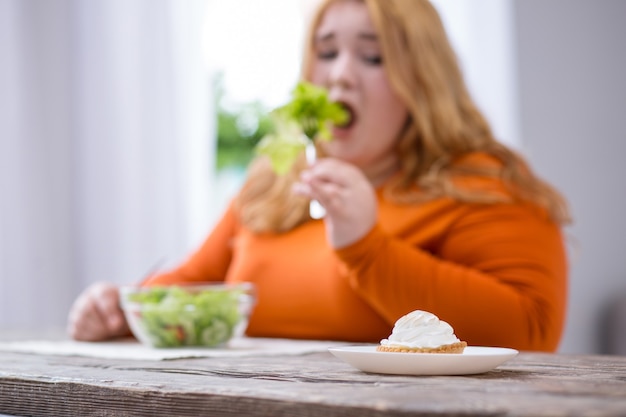 Mijn toetje. Troosteloze stevige vrouw die dessert bekijkt en gezond ontbijt heeft