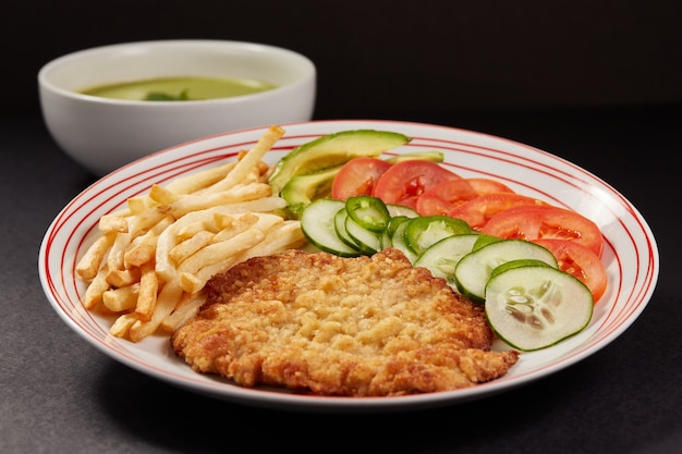 Milanesa de pollo con papas fritas y ensalada de pepino tomate y aguacate