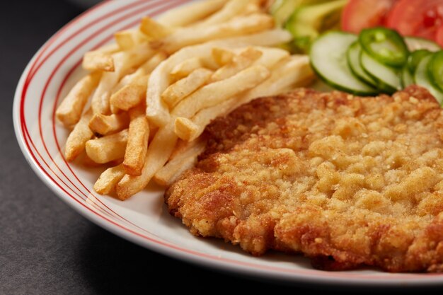 Milanesa de pollo met papas fritas en ensalada de pepino tomate en aguacate