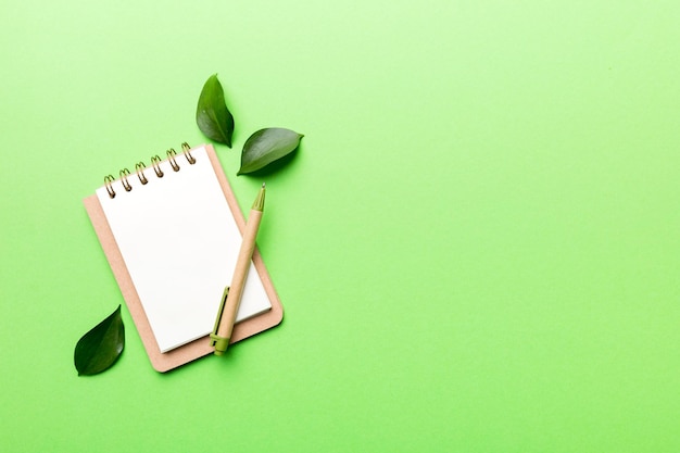 Milieuvriendelijk leeg notitieboekje met pen en groen blad op gekleurde achtergrond voor notitie