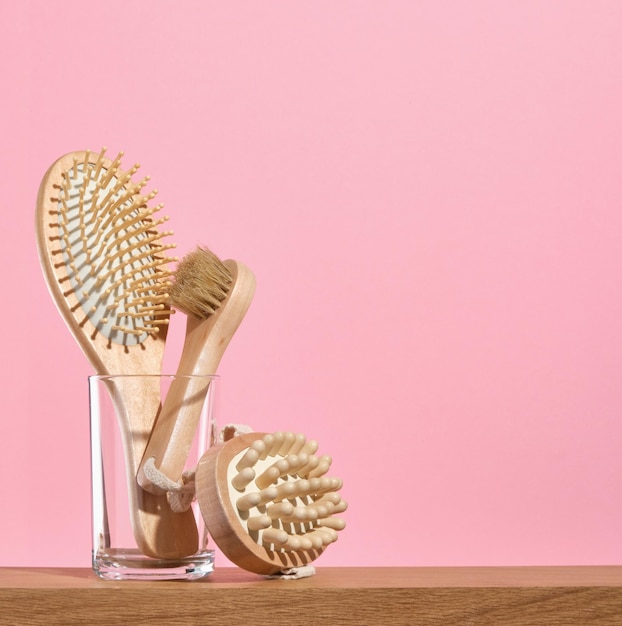 Milieuvriendelijke houten accessoires in glas op een roze achtergrond Houten haarborsel en borstels voor anticellulite-massage Kopieerruimte voor tekst