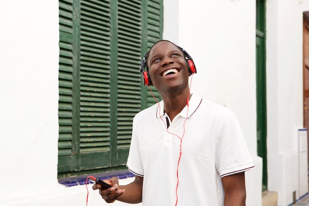 Miling young man listening to music with mobile phone and headphones outside