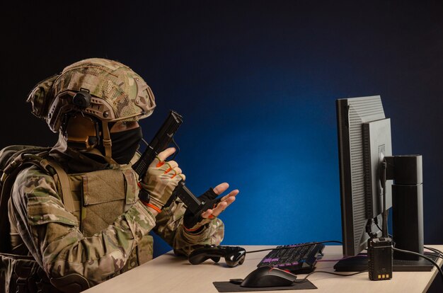 Militair in uniform zittend achter de computer leidt de cyberoorlogvoering met een pistool op de monitor