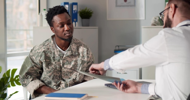 Foto militaire arts die xray bestudeert en een afro-amerikaanse soldaatpatiënt raadpleegt