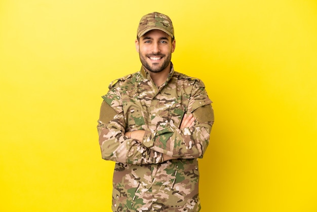 Militaire man geïsoleerd op gele achtergrond die de armen gekruist houdt in frontale positie