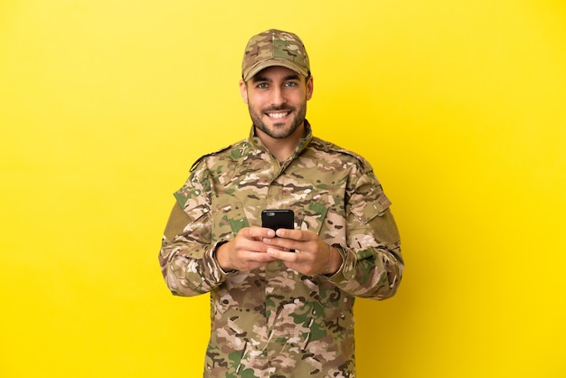 Militaire man geïsoleerd op gele achtergrond die een bericht verzendt met de mobiel