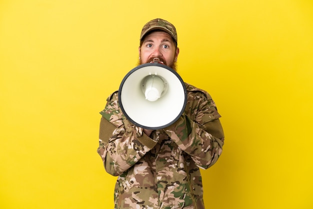 Militaire roodharige man over geïsoleerd op gele achtergrond schreeuwen door een megafoon