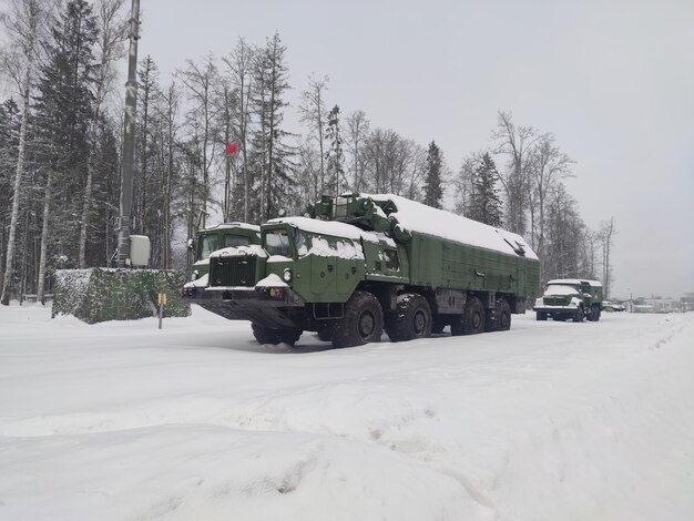 Militaire terreinwagen met een metalen frame en gesloten laadbak in de rijen van militair materieel in de winter tegen de achtergrond van het bos