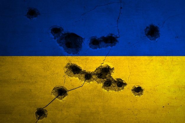 ウクライナの軍事紛争の背景コンクリートの壁に銃弾の穴と亀裂のある旗ロシアの侵略の概念写真