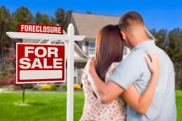 Military Couple Standing in Front of Foreclosure Sign and House