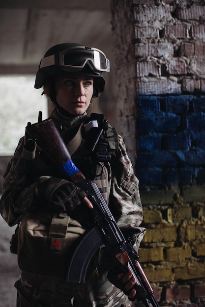 Military female soldier against the background of the flag of\
ukraine the flag of ukraine is painted on a brick wall a ukrainian\
defender with a weapon in his hands