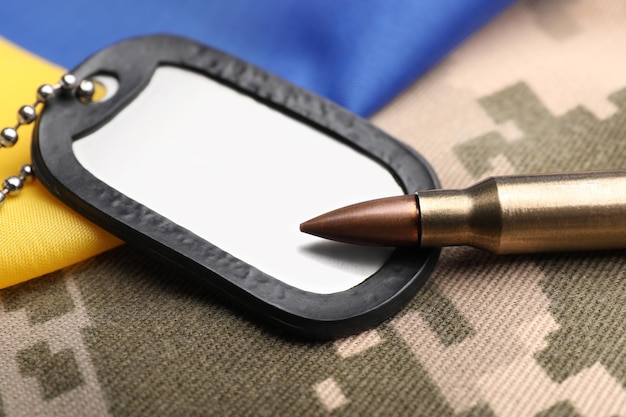 Military ID tag bullet and Ukrainian flag on pixel camouflage closeup