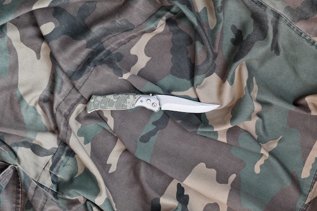 Military knife on army camouflage clothes close up. wall with copy space for military or special operations design