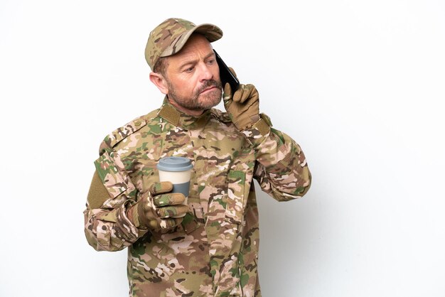 Фото Военный мужчина на белом фоне держит кофе на вынос и мобильный телефон