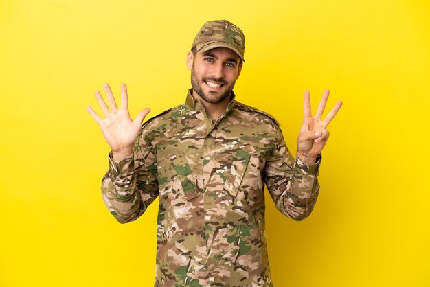 Militare isolato su sfondo giallo contando otto con le dita