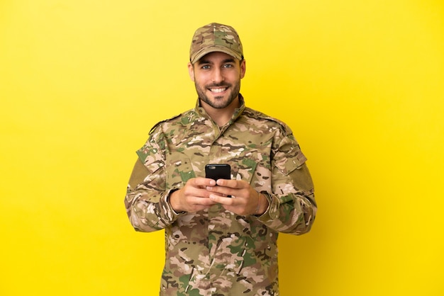 Military man isolated on yellow background sending a message with the mobile