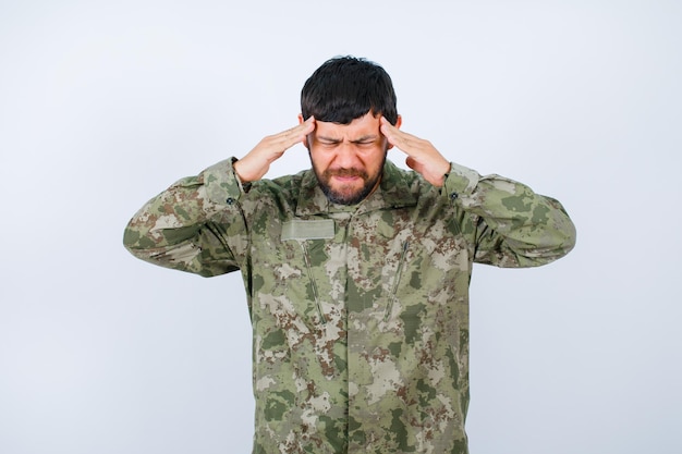 Military man with headache is holding hands on temples on white background