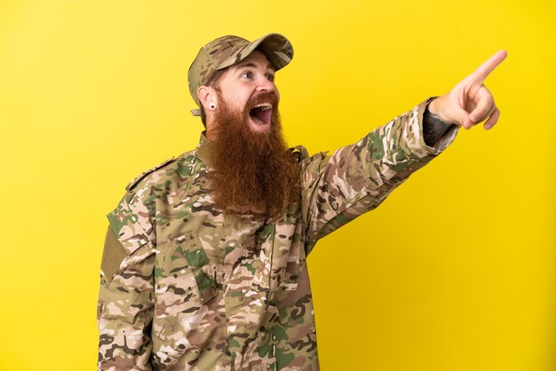 Military Redhead man over isolated on yellow background pointing away